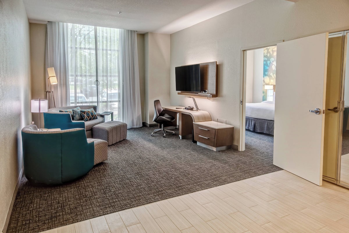 Ein Hotelzimmer mit Bett, Schreibtisch mit Stuhl, einer Couch und einem Fernseher an der Wand.