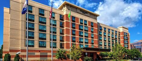 Un hotel Courtyard Marriott con fachada de ladrillo, múltiples ventanas y un área de entrada ajardinada.