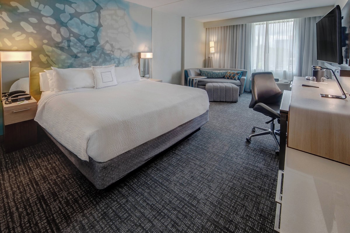 Ein Hotelzimmer mit einem großen Bett, einem Schreibtisch, einem Sessel, einer Couch und einem Fernseher.