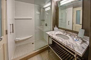 Un baño moderno con ducha envuelta en vidrio, lavamanos de mármol y un espejo grande.
