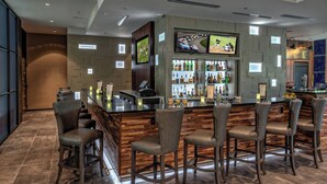 A bar area with a wooden bar counter, multiple bar stools, and a television mounted above the bar. - Courtyard by Marriott Dulles Airport Herndon (Herndon)