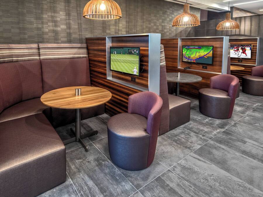 A modern lounge area with cushioned seating, a round table, and two televisions displaying sports.
