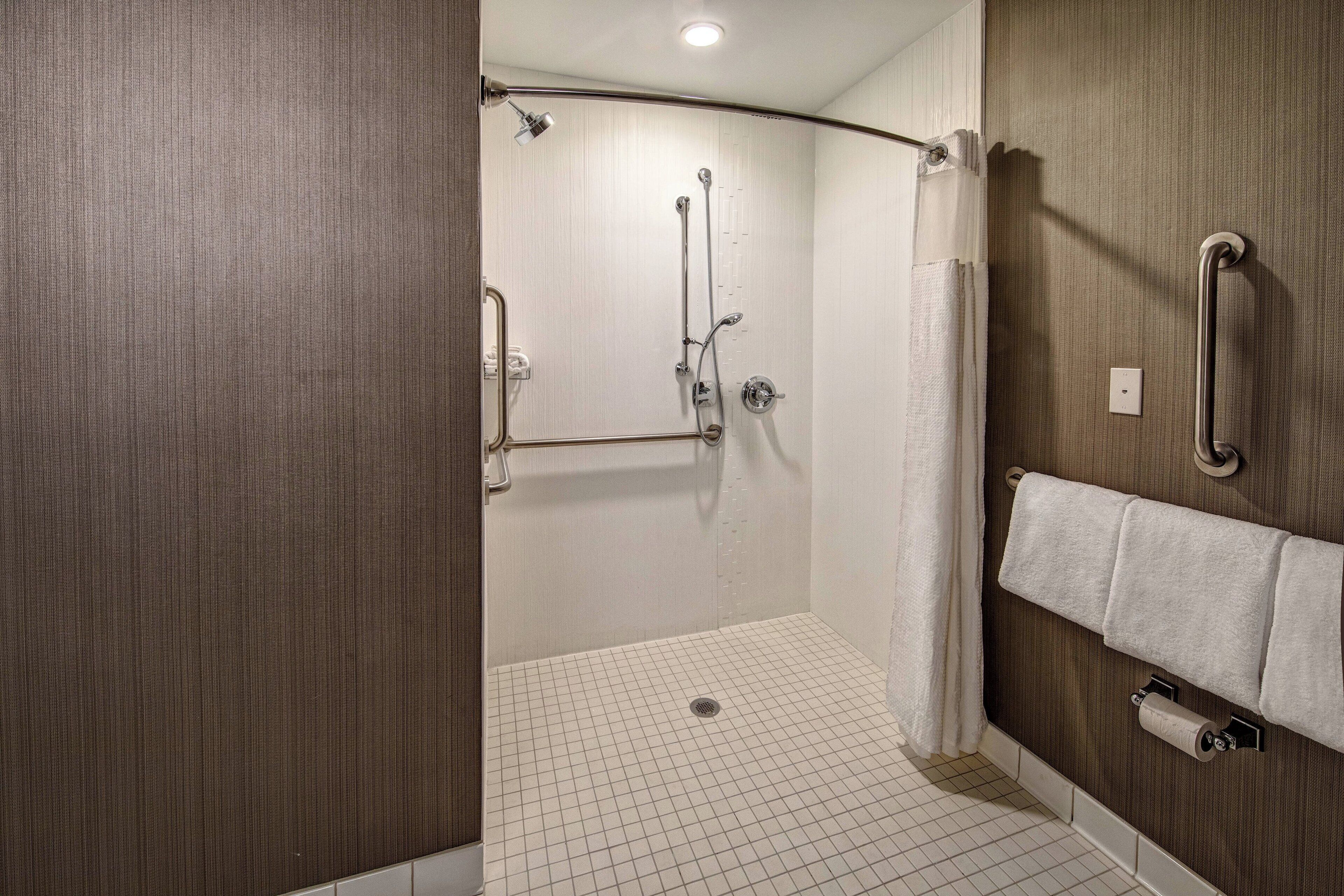 Un baño moderno con cabina de ducha, barras de apoyo y un perchero para toallas.