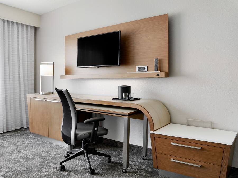 Quarto de hotel com escrivaninha, cadeira, televisão e abajur.