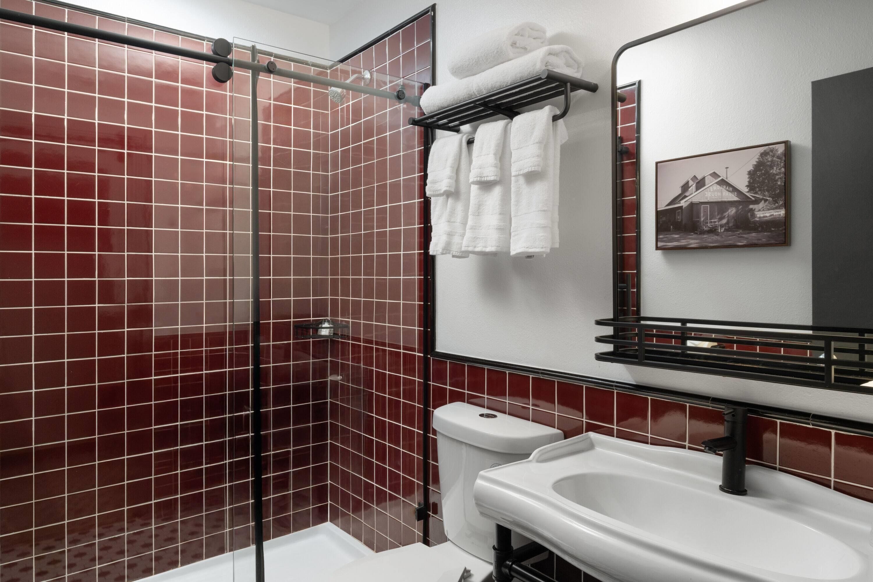 A bathroom with a glass shower enclosure, a white sink, and a toilet. There are towels hanging on a rack above the sink.