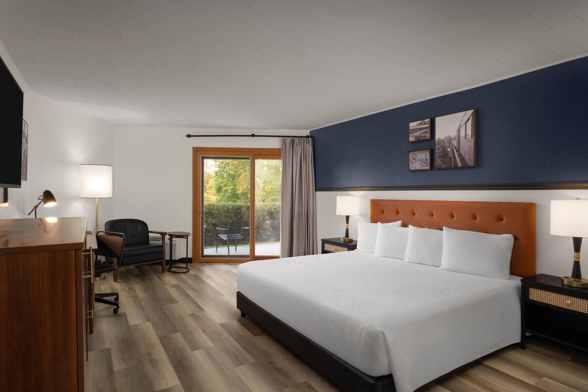 A hotel room with a large bed, a desk, a chair, and a view of the outdoors.