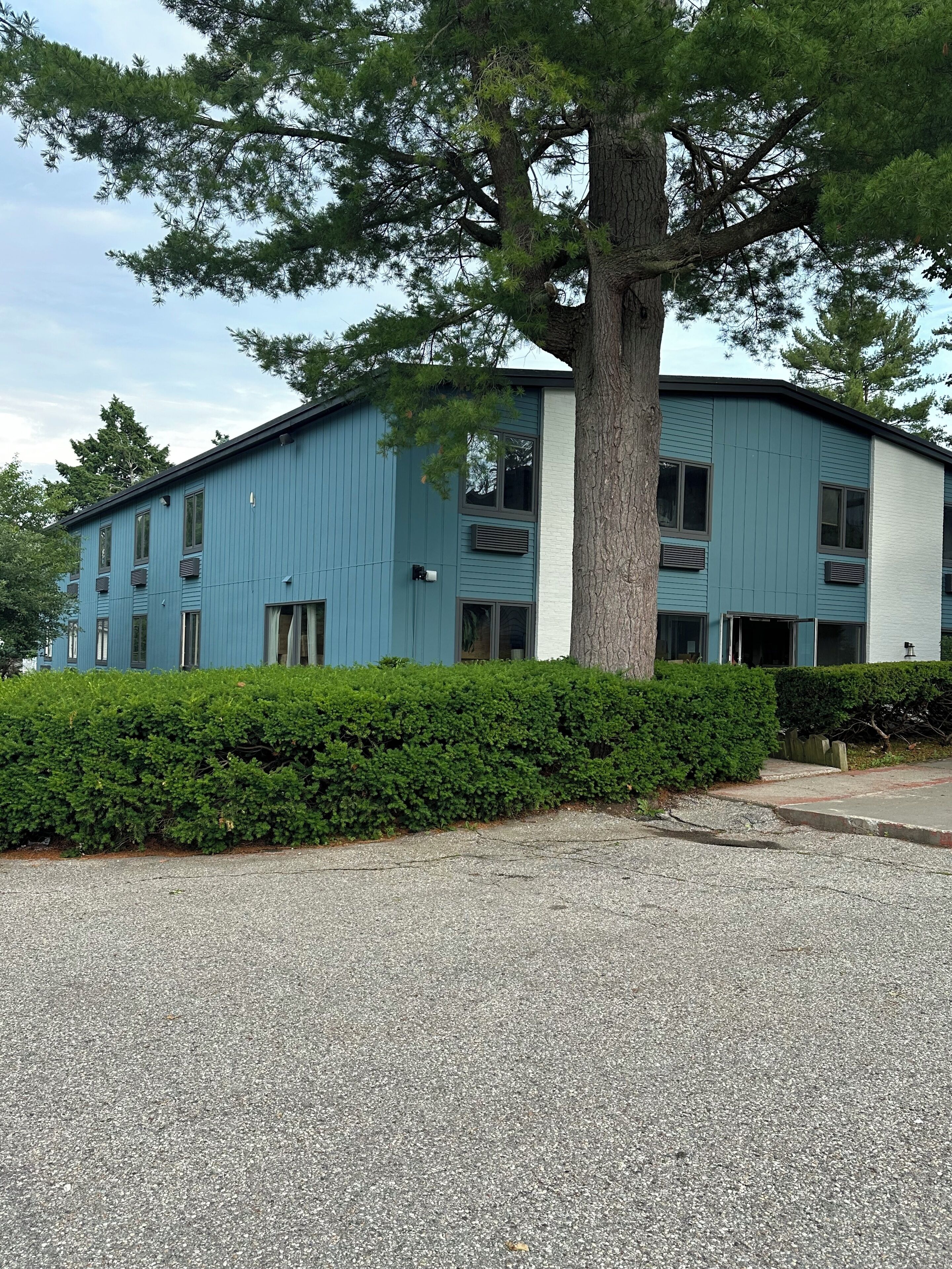 A two-story building with a blue exterior and a large tree in front.