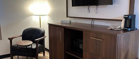 Una habitación de hotel con un escritorio de madera, una silla, un televisor montado en la pared y una mesita de noche con lámpara.
