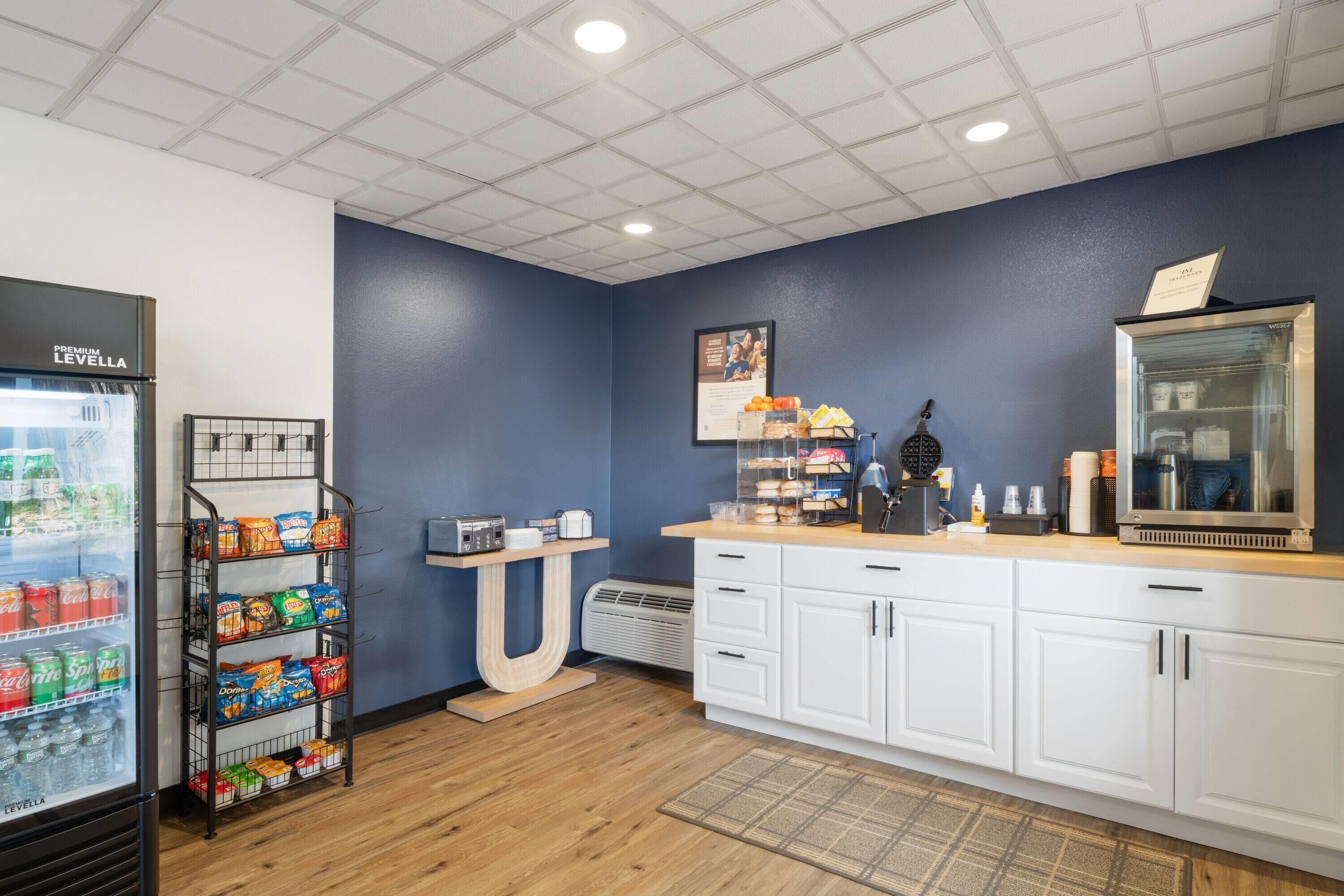 Una kitchenette con un refrigerador lleno de bebidas, un estante con botanas, una cafetera y un microondas.