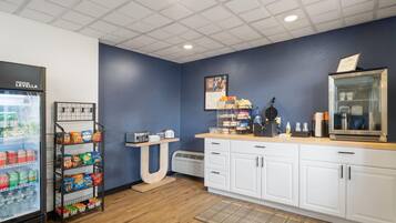 Una kitchenette con un refrigerador lleno de bebidas, un estante con botanas, una cafetera y un microondas.