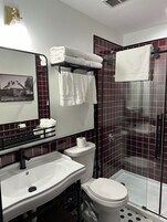 Un baño con lavamanos blanco, inodoro, cabina de ducha de vidrio y espejo con marco.
