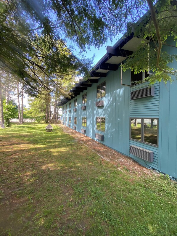 A row of light blue buildings with multiple windows and air conditioning units, surrounded by a grassy area and trees. - Hotel Vervana, Trademark Collection by Wyndham (Bennington)