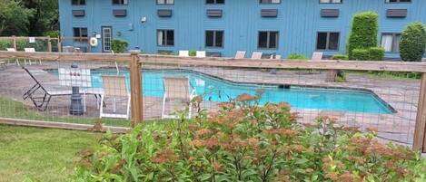 Un edificio azul con piscina, rodeado de vegetación y árboles.