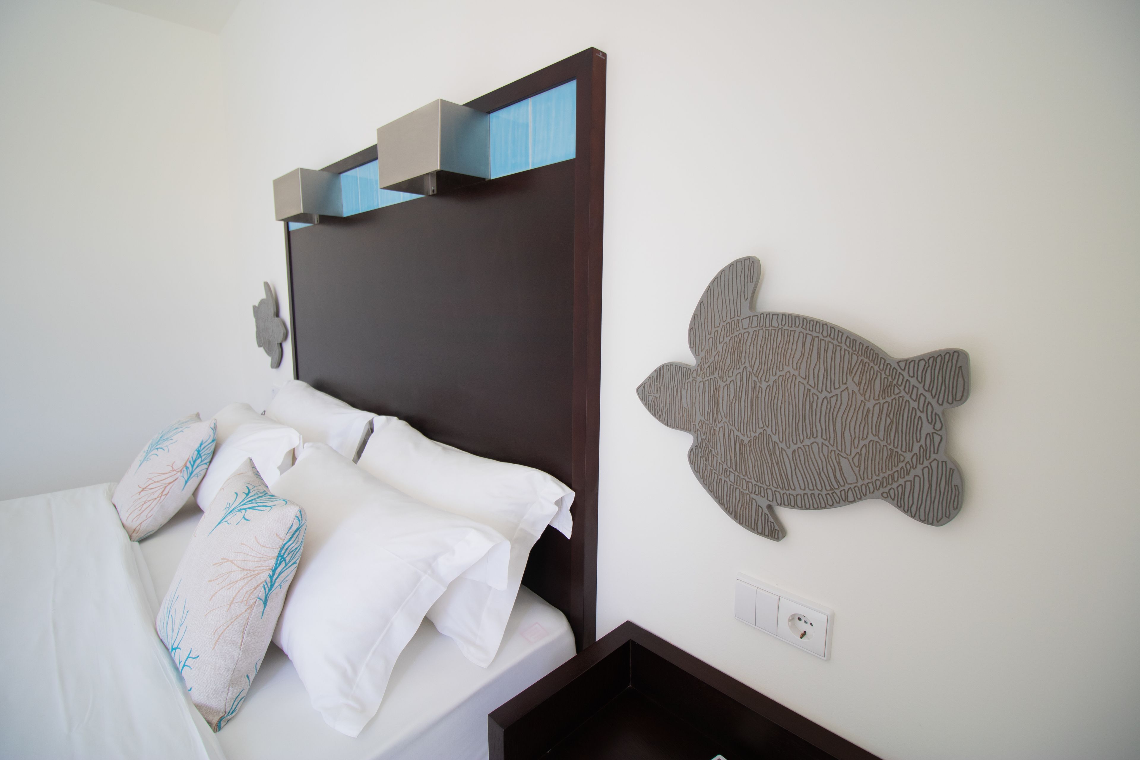 A neatly made bed with white linens and decorative pillows, a dark wooden headboard, and a wall-mounted turtle decoration.