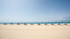 A beach with rows of sun loungers under white canopies, facing the ocean. - Hotel Dunas de Sal (Sal)