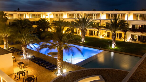 A hotel with a swimming pool, palm trees, and outdoor seating areas. - Hotel Dunas de Sal (Sal)