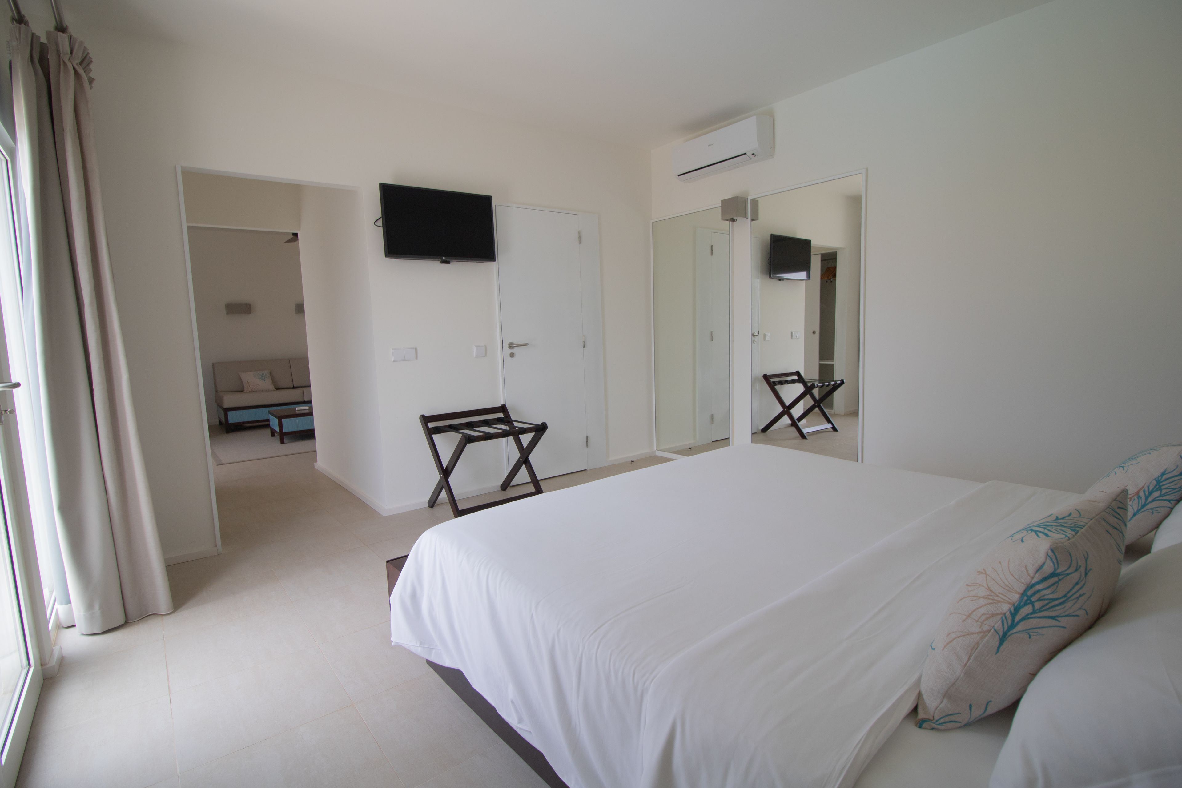 A bedroom with a large bed, a TV mounted on the wall, a mirror, and a wardrobe.