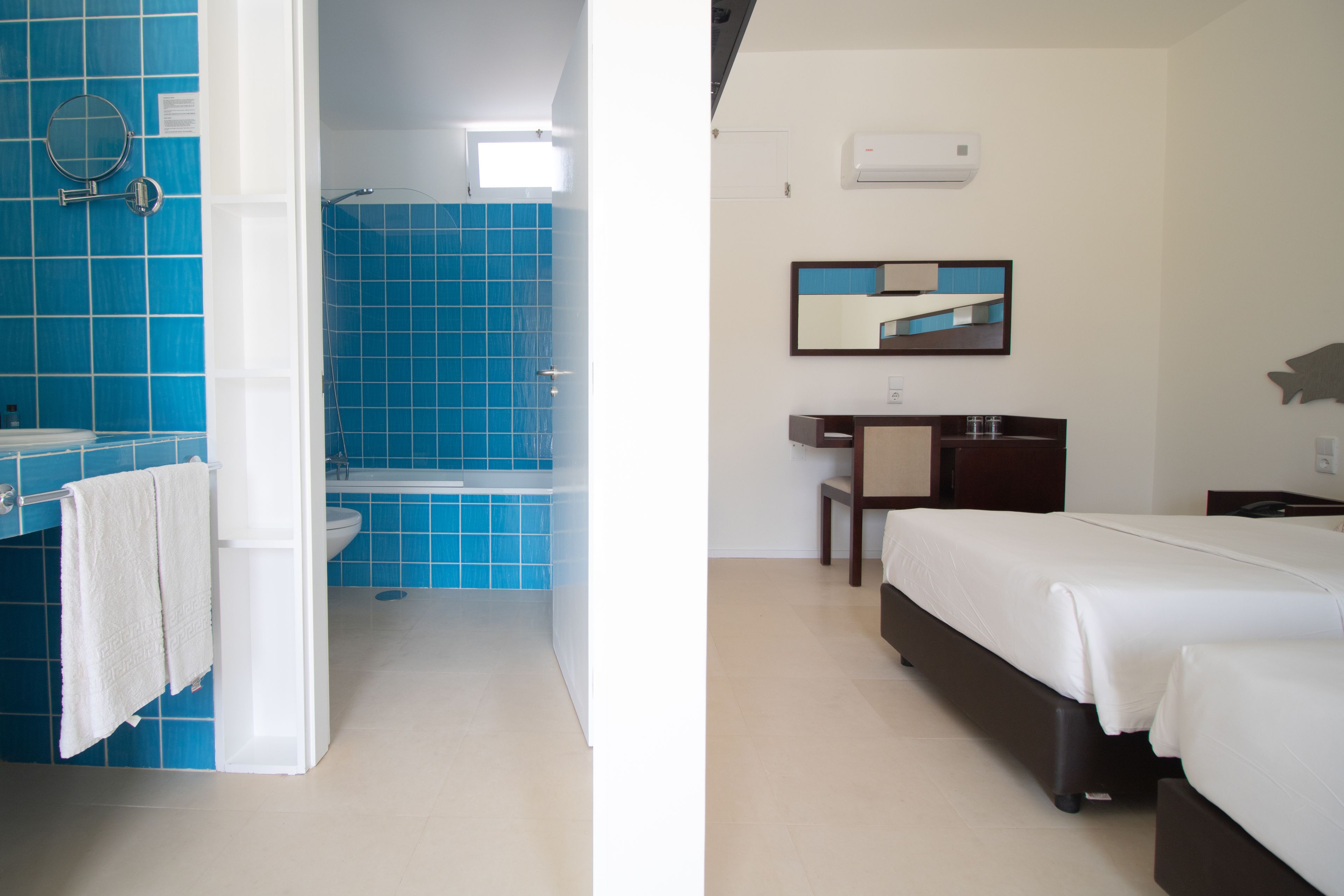 Un baño con azulejos azules, un lavamanos y un espejo. El baño tiene una puerta blanca y una toalla blanca colgada en la pared.