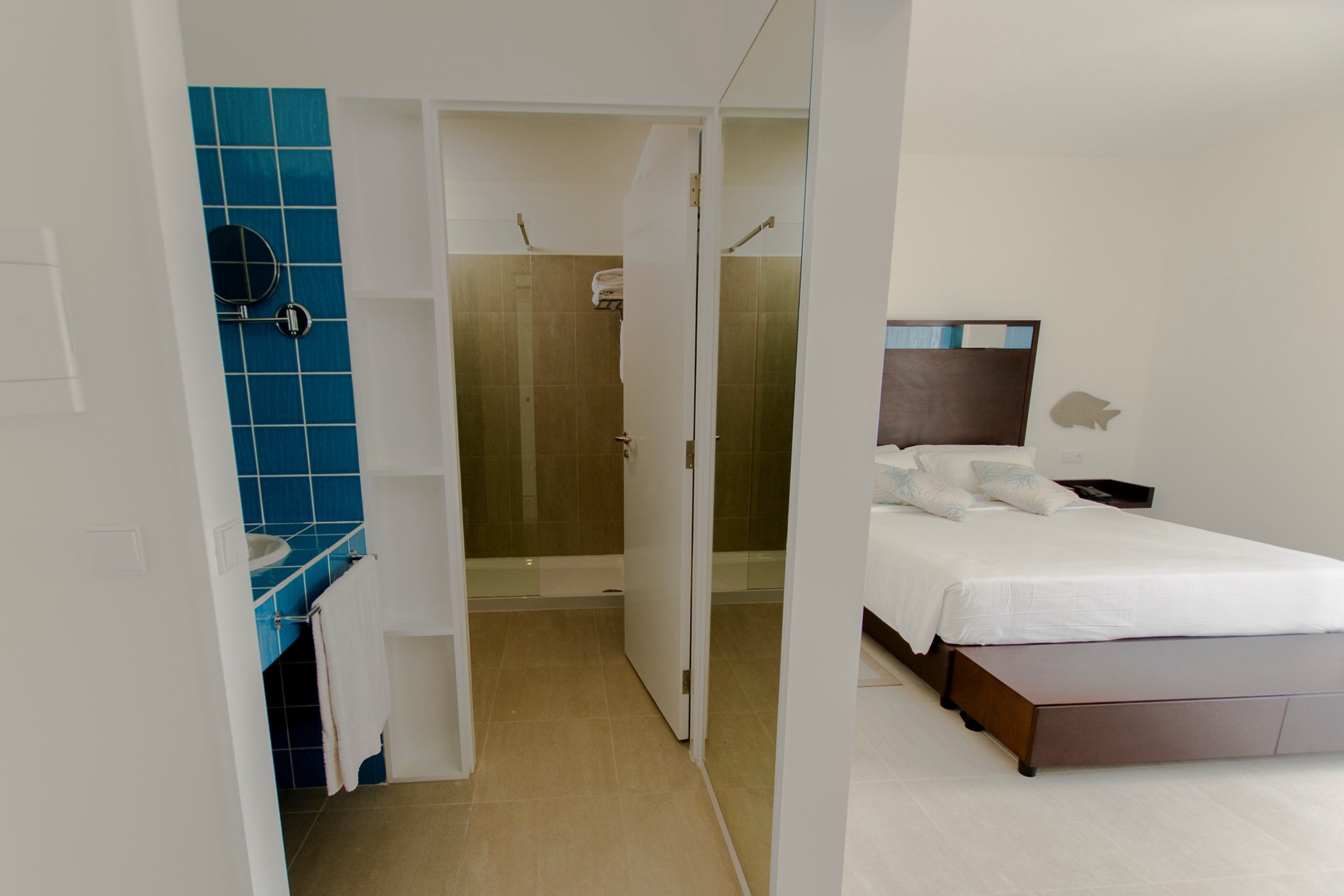 A hotel room with a bed, a bathroom with a blue-tiled shower, and a white sink.