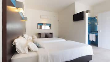 A modern hotel room with a large bed, a flat-screen TV mounted on the wall, a small desk, and a bathroom with blue tiles.