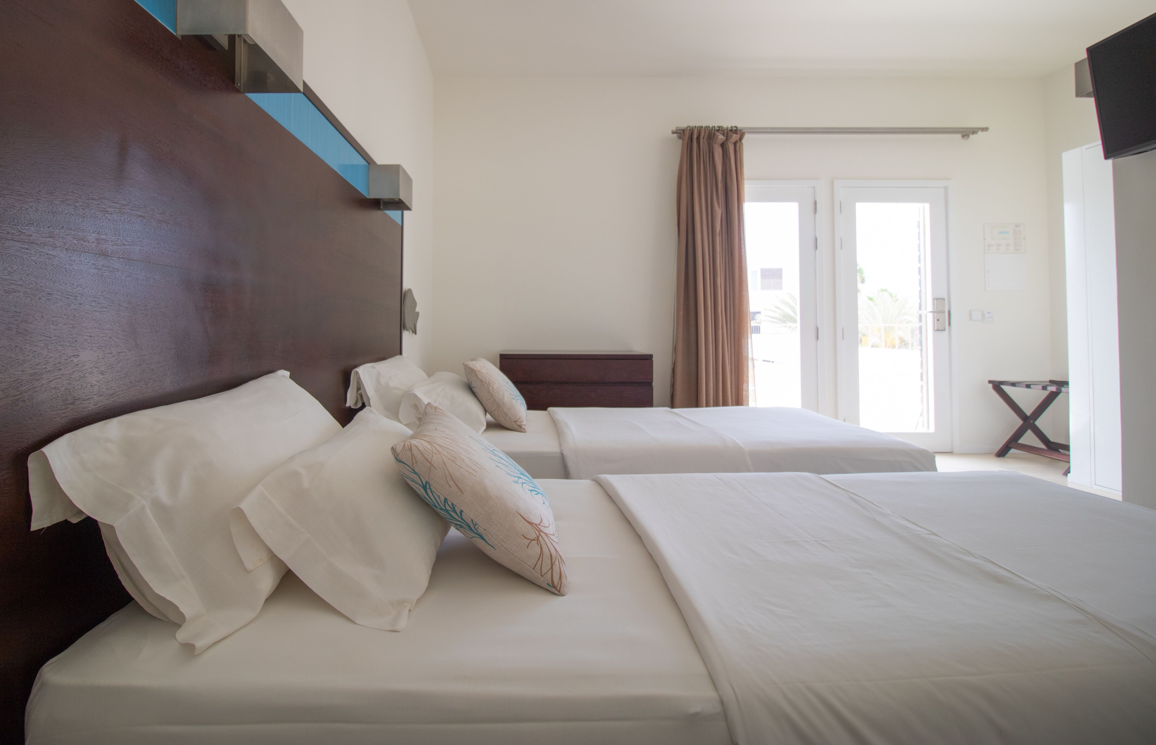 A hotel room with two beds, a wooden headboard, and a view of the outdoors through a door.