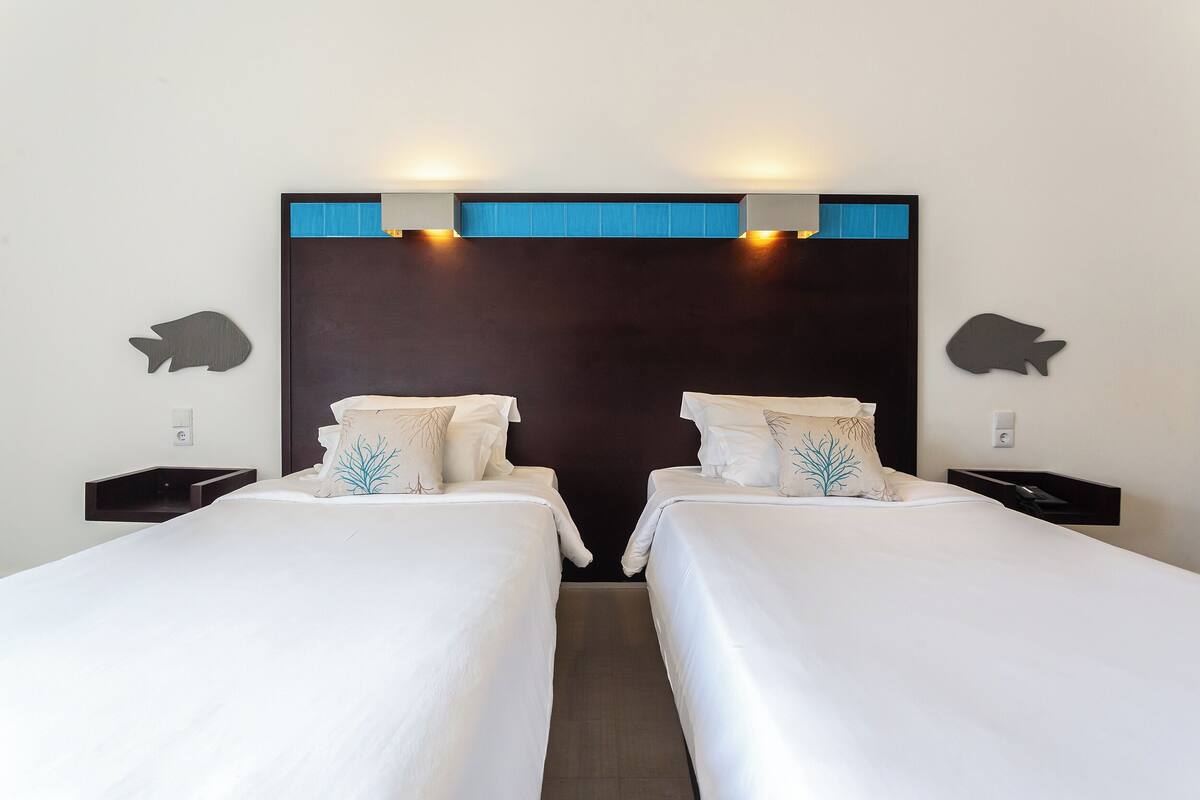A hotel room with two single beds, a dark headboard, and wall-mounted nightstands.