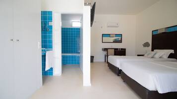 Habitación de hotel con dos camas, baño con azulejos azules, televisor de pantalla plana y una mesita.