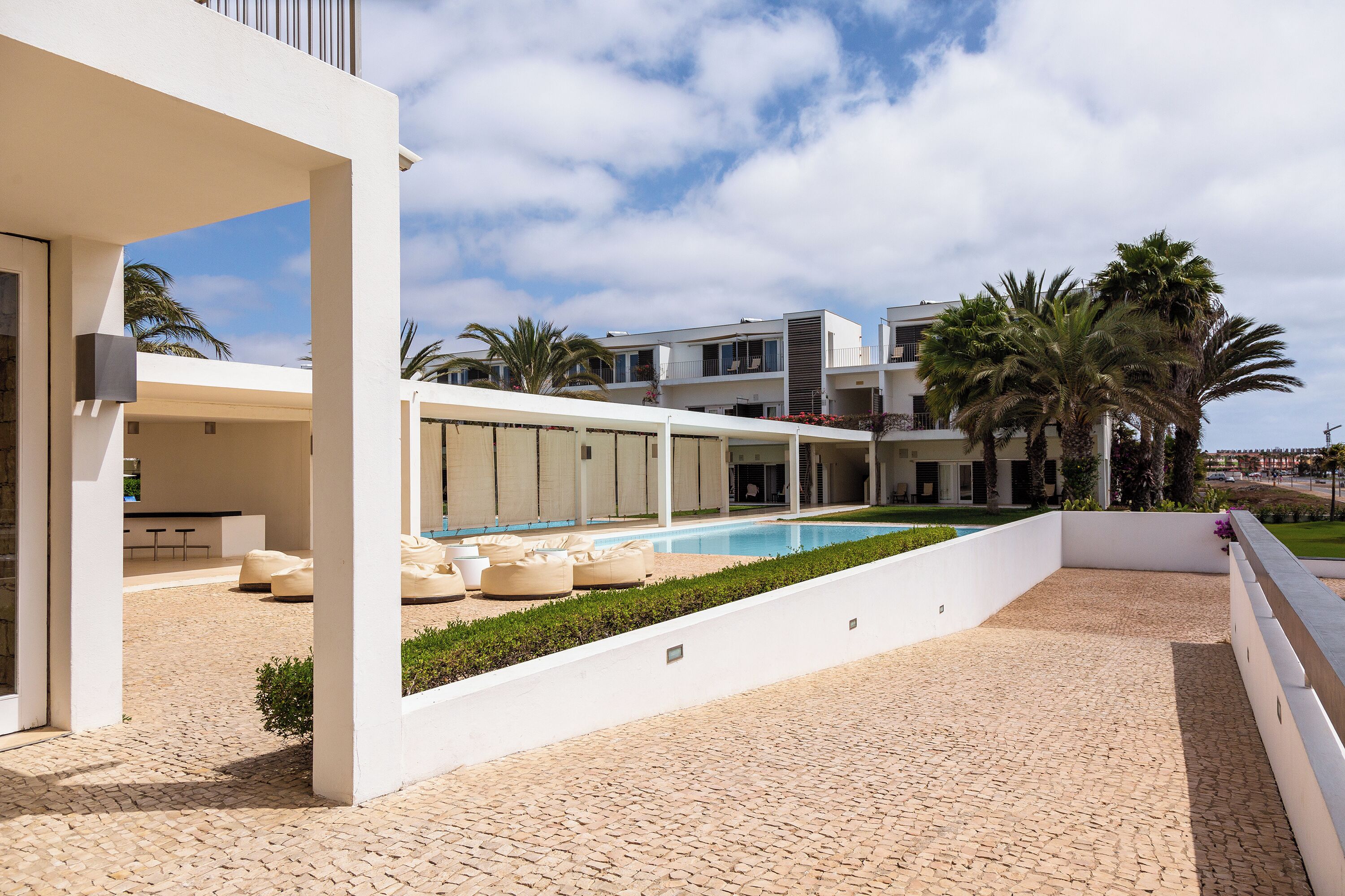 A modern building with a pool, outdoor seating, and palm trees.