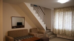Ein Wohnzimmer mit Sofa, Hocker, Couchtisch und einer Treppe, die zu einer oberen Etage führt.
