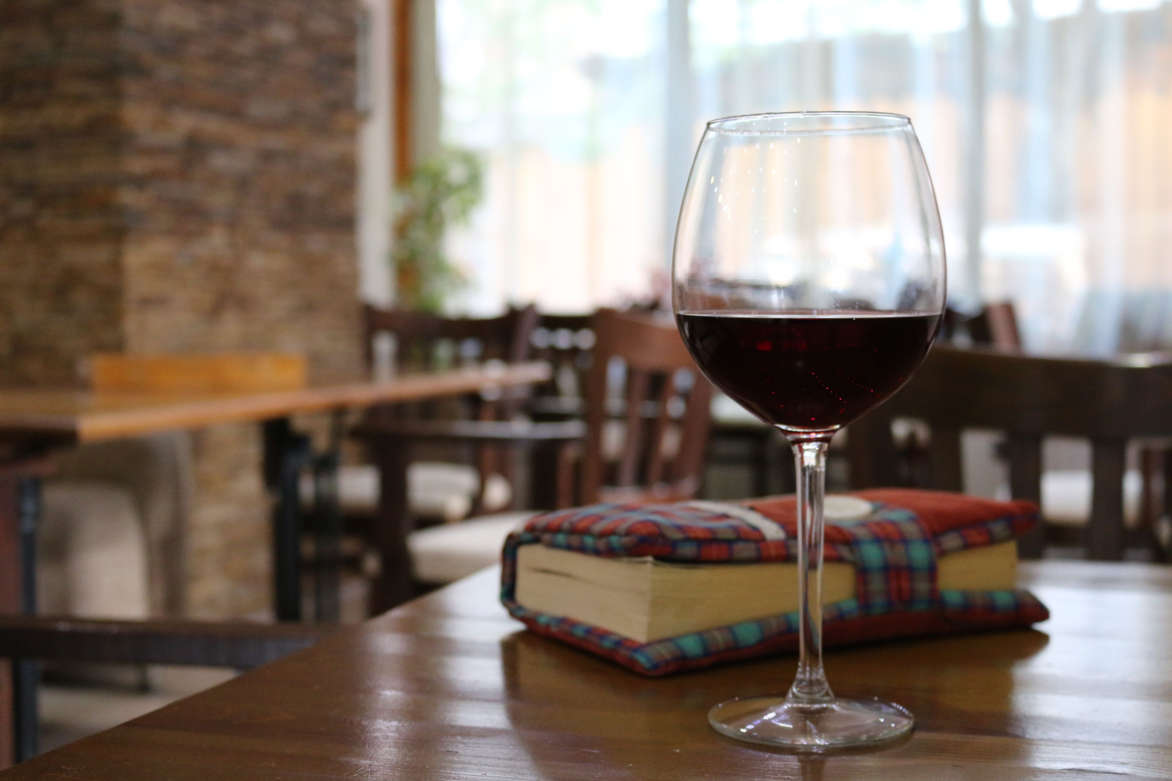 Una copa de vino tinto sobre una mesa de madera, con un libro a cuadros a su lado.