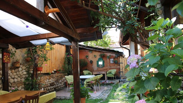 Eine Terrasse mit Steinfliesen, Holztischen und -stühlen sowie Blumentöpfen.