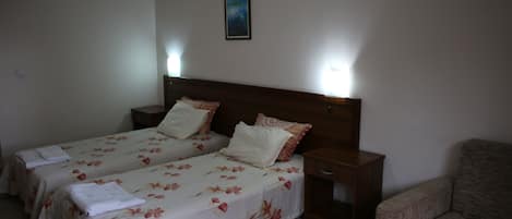 Habitación de hotel con dos camas individuales, una mesita de noche de madera, una mesa de madera y un sofá.