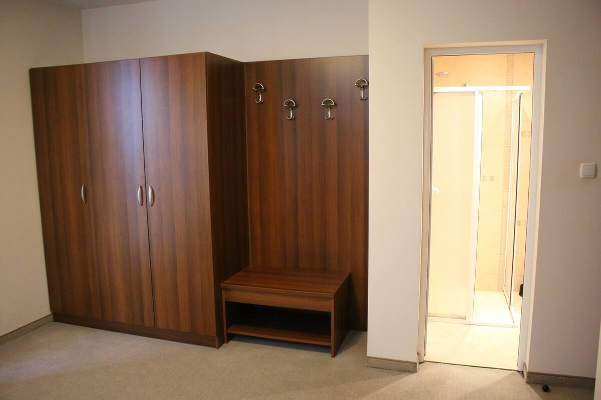 Quarto com um guarda-roupa espaçoso, um pequeno banco e uma porta que dá para outro cômodo.