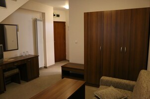 A room with a wooden desk, a sofa, a wardrobe, and a shower area.