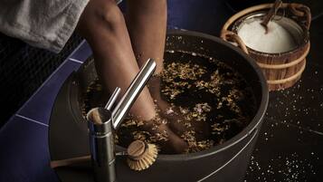 A bathtub filled with water and bath salts, a wooden brush, and a metal container.