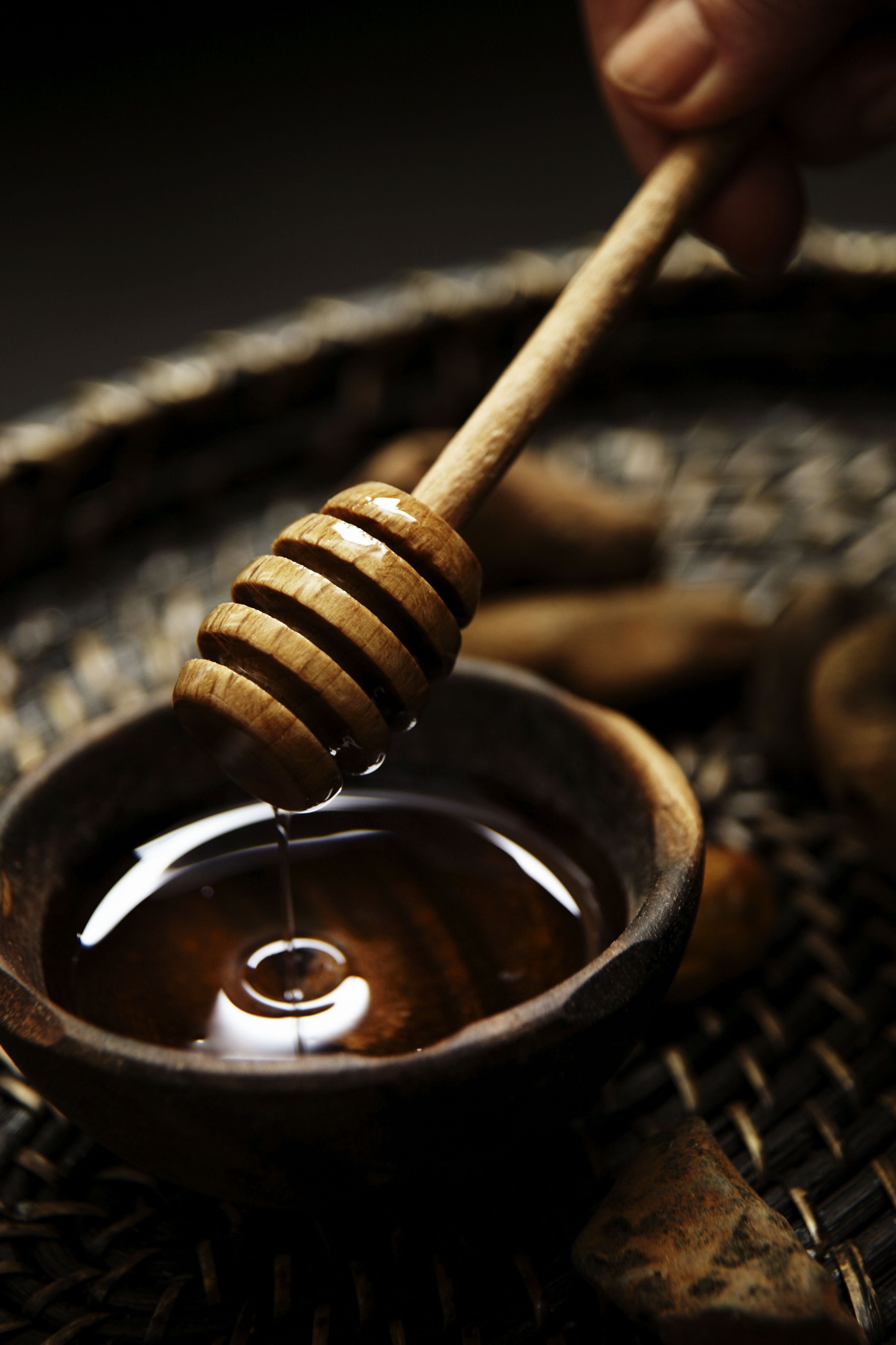 A wooden honey dipper dripping honey into a rustic bowl.