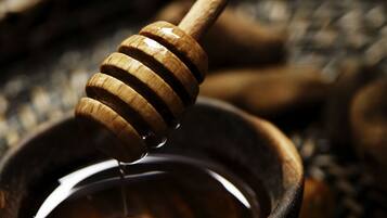 A wooden honey dipper dripping honey into a rustic bowl.