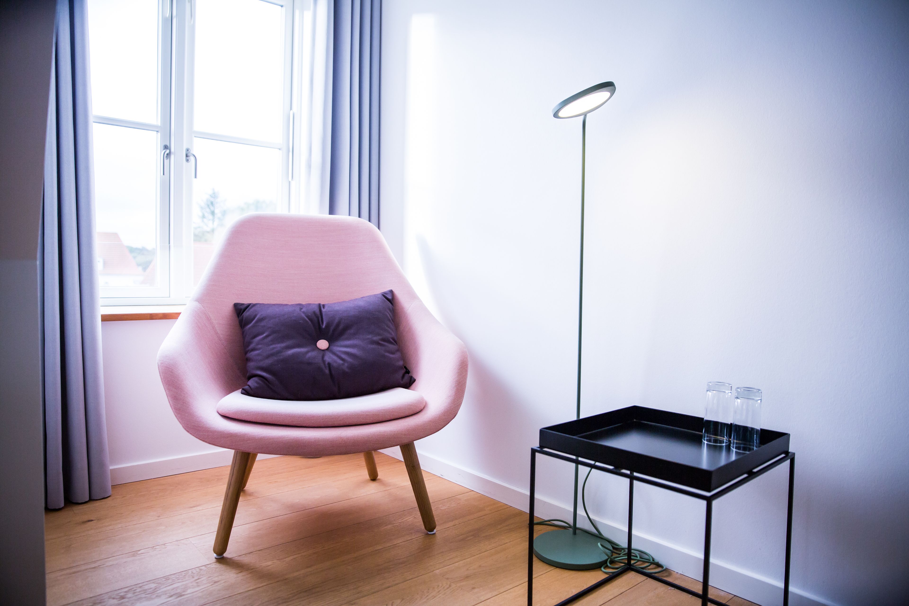 A modern room with a pink chair, a small black table, and a floor lamp.