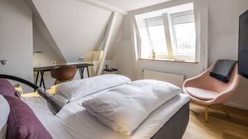 A modern bedroom with a bed, a chair, a desk, and a window.