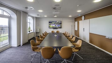 Une salle de conférence avec une longue table, de nombreuses chaises, un grand écran et une horloge au mur.