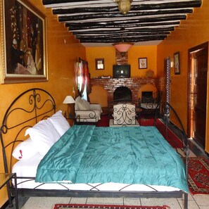 A bedroom with a bed, a fireplace, a television, and a painting on the wall. - L' Arganier D'or (Ait Igas)
