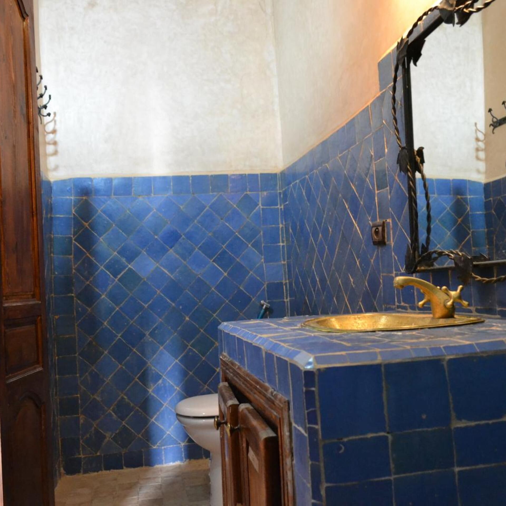 A bathroom with blue patterned tiles, a wooden door, a white toilet, and a gold faucet.