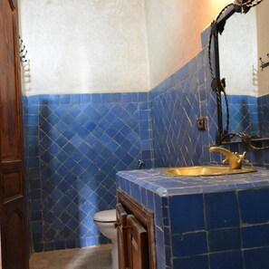 A bathroom with blue patterned tiles, a wooden door, a white toilet, and a gold faucet. - L' Arganier D'or (Ait Igas)