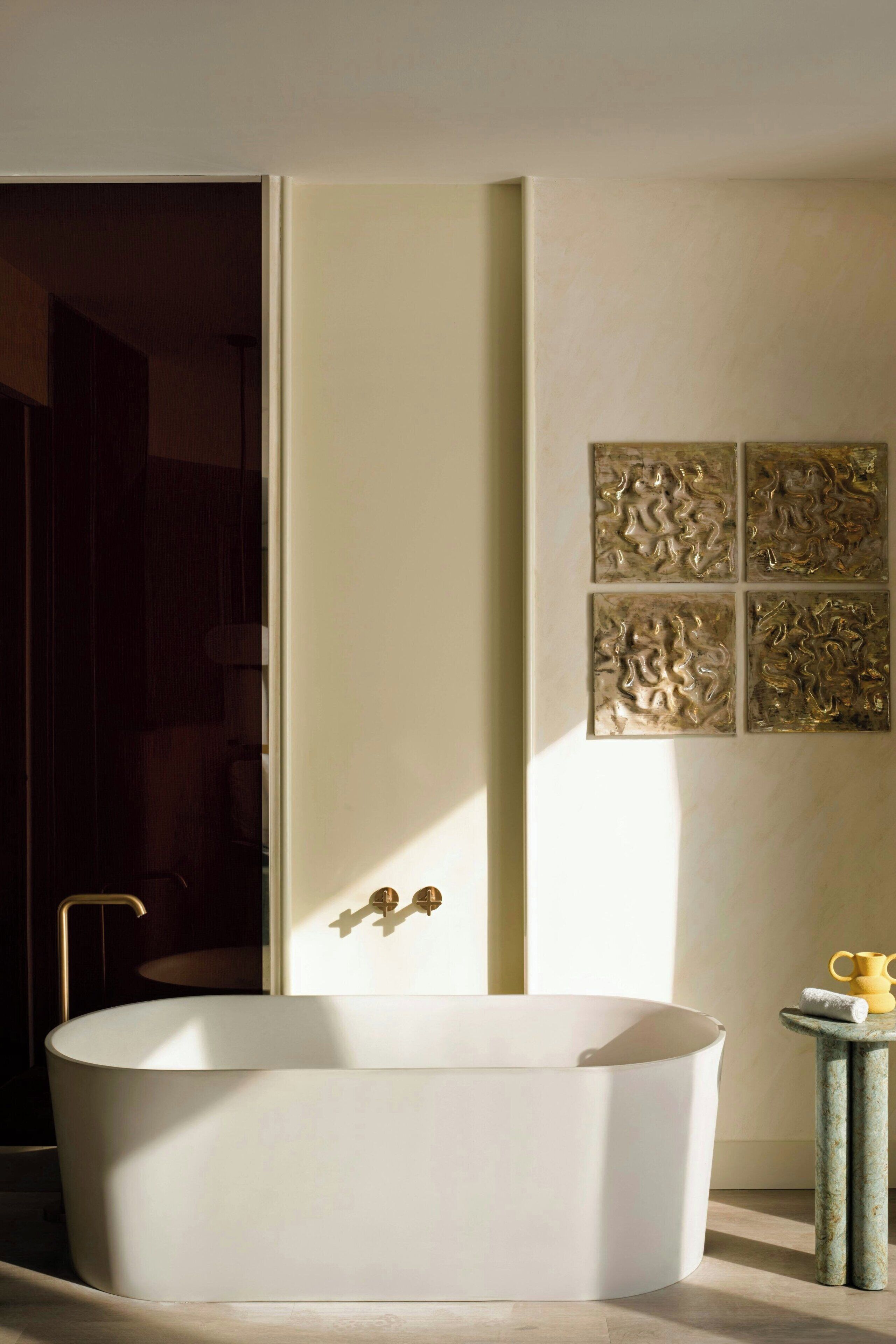 A modern bathroom with a freestanding bathtub, a small round table with a towel, and a wall-mounted light fixture.