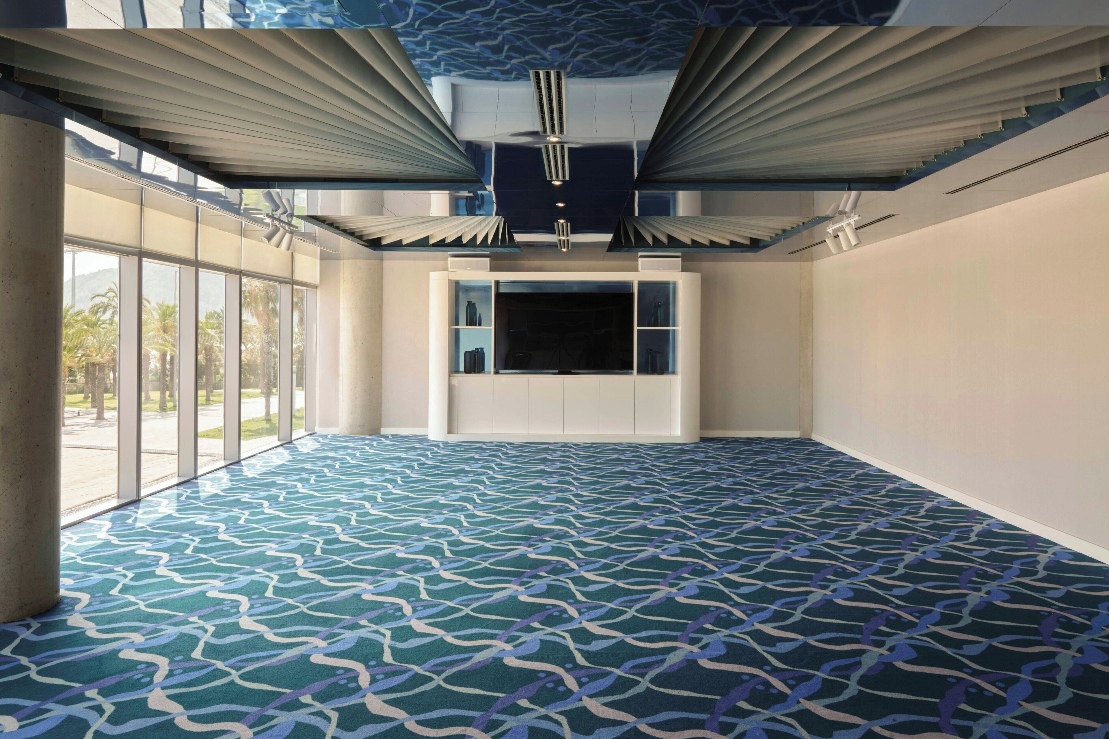 A spacious room with a patterned carpet, large windows, and a ceiling with a unique design.
