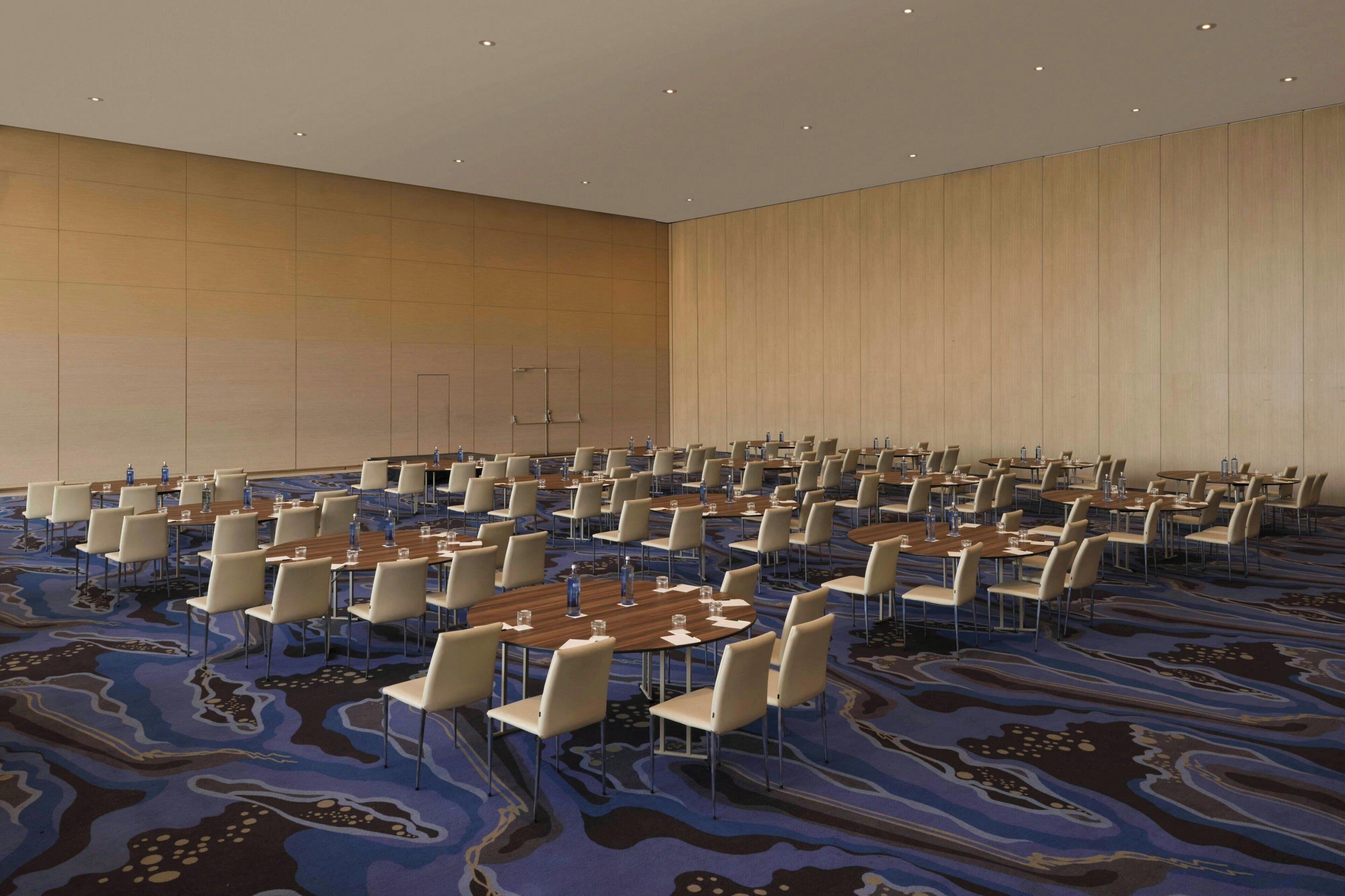A large conference room with multiple tables and chairs, a patterned carpet, and wooden panel walls.