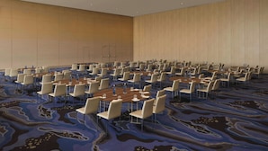 Un amplio salón de conferencias con varias mesas y sillas, una alfombra estampada y paneles de madera.