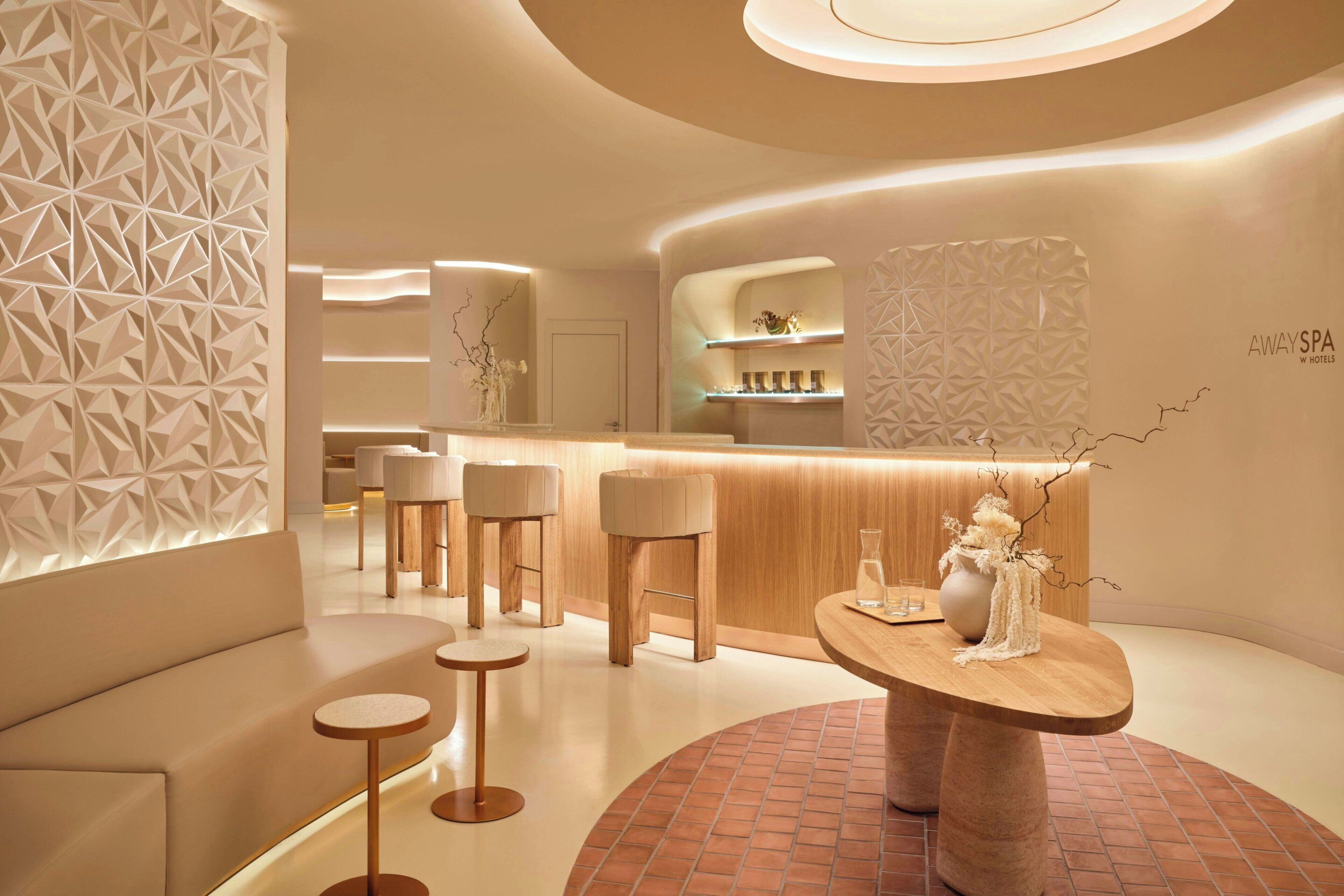 Un salón moderno y bien iluminado con un mostrador de recepción curvo, arreglos de asientos y elementos decorativos.