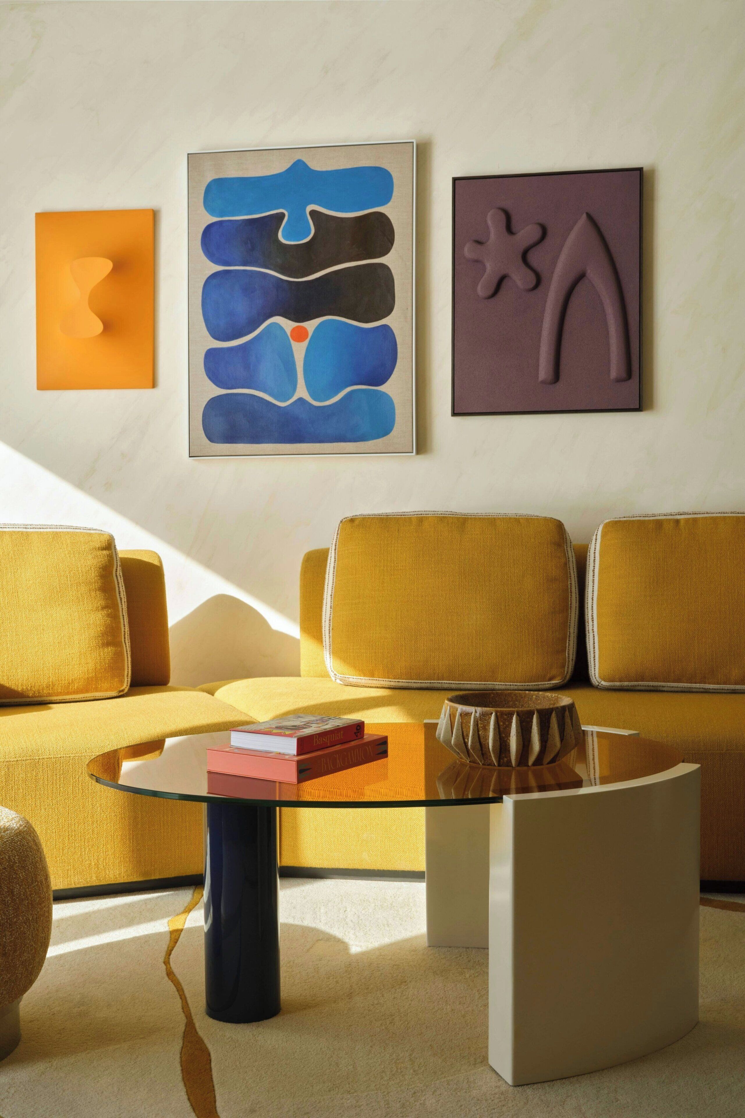 Una sala de estar moderna con un sofá, una mesa de centro de vidrio y arte abstracto en la pared.