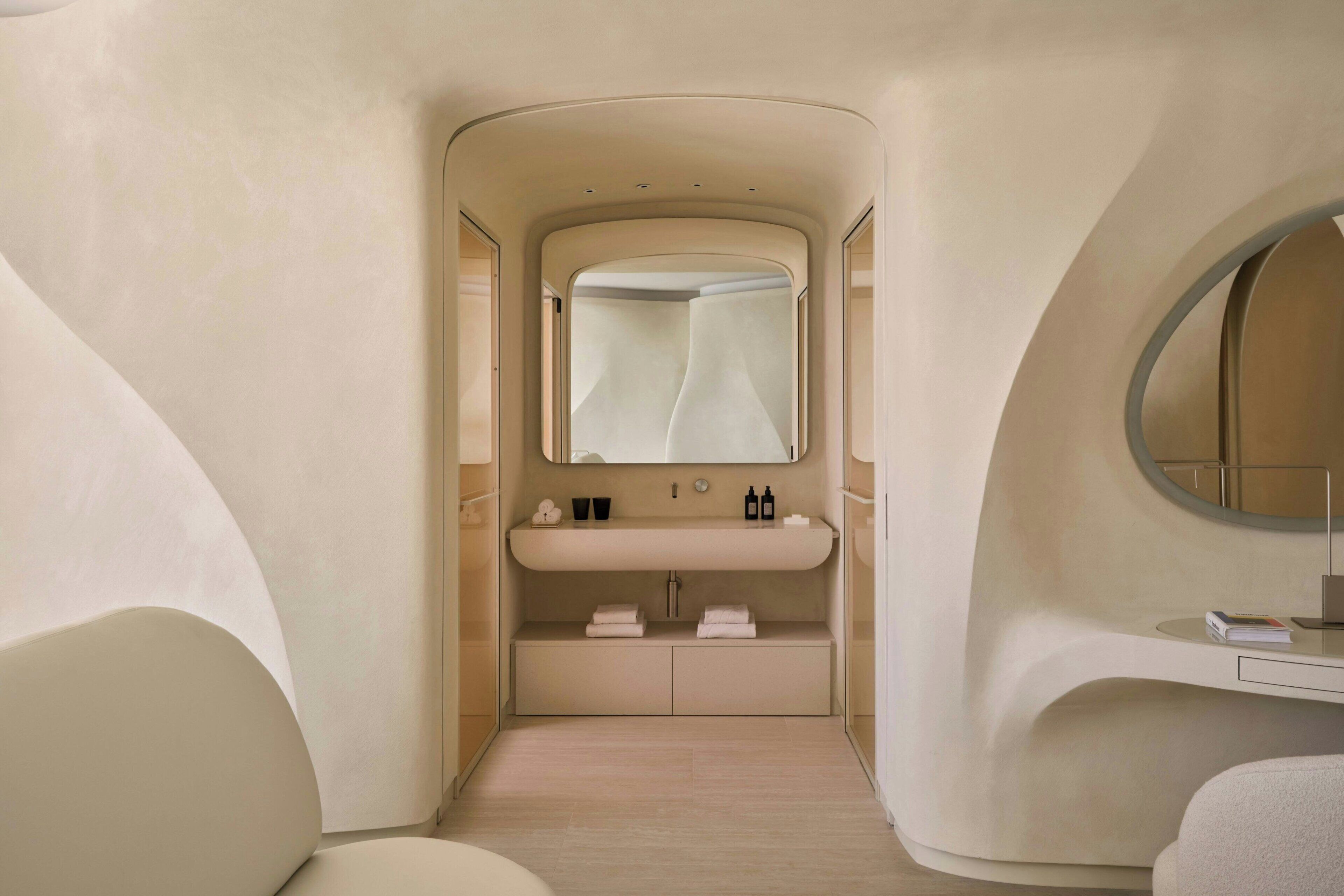 Un baño moderno con diseño curvo, un tocador con espejo y una pequeña zona de estar.